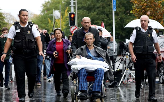 Temel Atacocugu (c), a survivor of the  mosque attacks, leaves the Christchurch District Court after the alleged gunman's second court appearance.