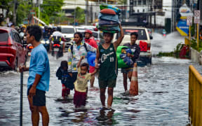 Residents carrying their belongings, wade through a flooded street in Mandaue City, Cebu province on November 4, 2025, after Typhoon Kalmaegi hit overnight. Residents sought refuge on rooftops and cars floated through flooded streets on November 4 as Typhoon Kalmaegi battered the central Philippines, leaving at least two people dead. (Photo by Alan TANGCAWAN / AFP)