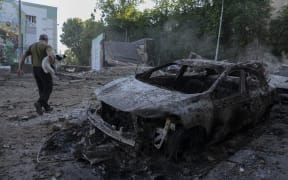A man carrying a dog walks past the wreckage of cars following mass Russian drones and missile strike on the Ukraine's capital Kyiv on July 4, 2025, amid the Russian invasion of Ukraine. Kyiv said on July 4 that Russia had launched its largest overnight aerial attack on Ukraine over the more than three-year invasion. A representative of Ukraine's air force Yuriy Ignat said the barrage of 550 drones and missiles was a record, adding "this is the largest number that the enemy has used in a single attack." (Photo by OLEKSII FILIPPOV / AFP)