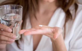 Woman holding pill and glass of water in hands taking emergency medicine, supplements or antibiotic antidepressant painkiller medication to relieve pain, meds side effects concept, close up view