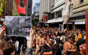 John Miller's photograph of the 1975 land march held up in the same location at the 2024 Hīkoi in Pōneke Wellington