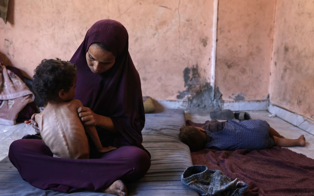 Naeema, a 30-year-old Palestinian mother, sits with her malnourished 2-year-old son Yazan in their damaged home in the Al-Shati refugee camp, west of Gaza City, on July 23, 2025. More than 100 aid organisations and human rights groups warned on Wednesday that "mass starvation" was spreading in Gaza, as the United States said its top envoy was heading to Europe for talks on a possible ceasefire and aid corridor. (Photo by Omar AL-QATTAA / AFP)