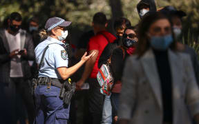 A New South Wales police officer wearing a face mask talks with people as they stand in a line waiting to be vaccinated at the Sydney Olympic Park Vaccination Centre at Homebush in Sydney on August 16, 2021. (Photo by DAVID GRAY / AFP)