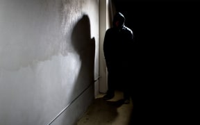 hooded criminal stalking in the shadows of a dark street alley alleyway