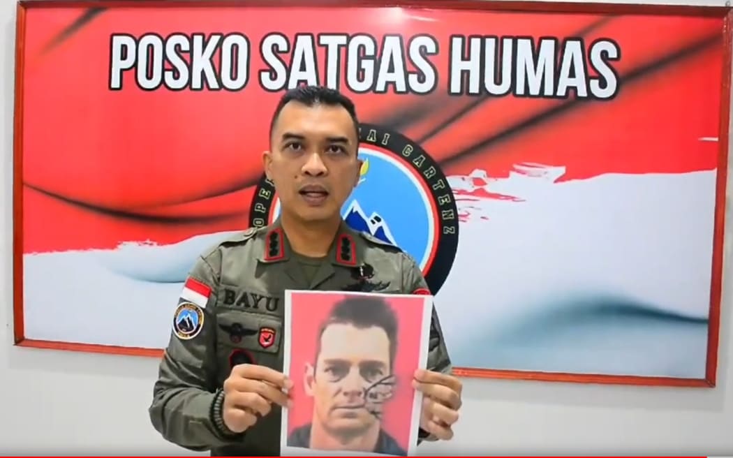 An Indonesian police spokesperson holds up a photo of Glen Malcolm Conning in a video.