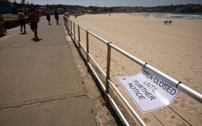 People walk past an empty Bondi Beach after authorities closed Sydney's most popular beach on March 22, 2020. Bondi Beach was closed after huge crowds flocked to the popular sunbathing spot despite a government ban on large gatherings due to the coronavirus pandemic.