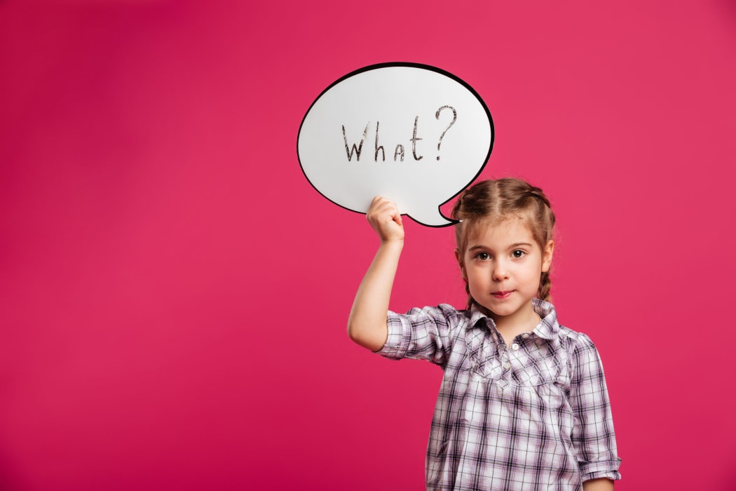 Image of pretty little girl child standing isolated over pink background. Looking camera holding speech bubble.