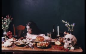 Singer and author Michelle Zauner poses leaning on a wooden table which is spread with a skull, candle and various food items.