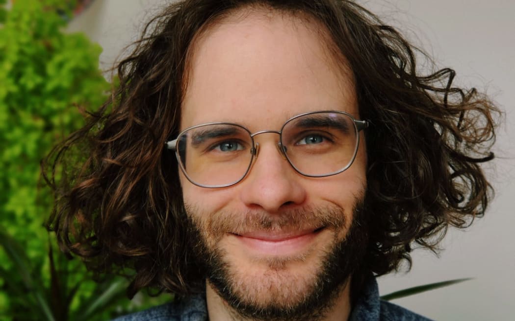 Mid-shot of NPR Podcast host Darian Woods who has long curly hair and wears glasses