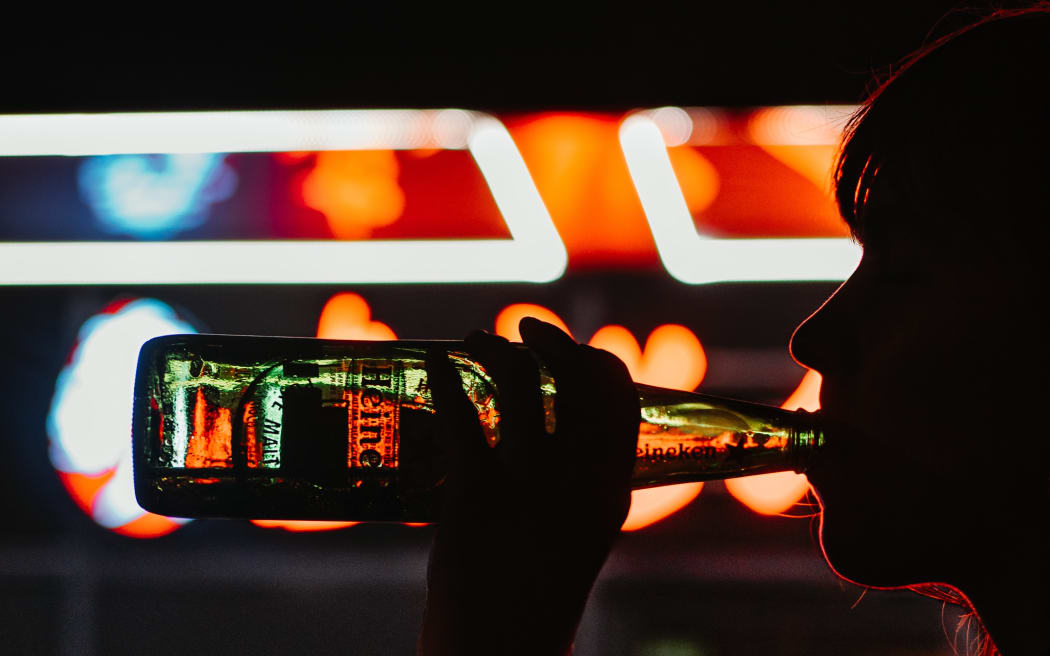 A person in silhouette drinking a bottle of alcohol with bright lights behind them.