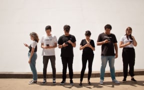 A line of teenagers standing outside all studying their mobile phones