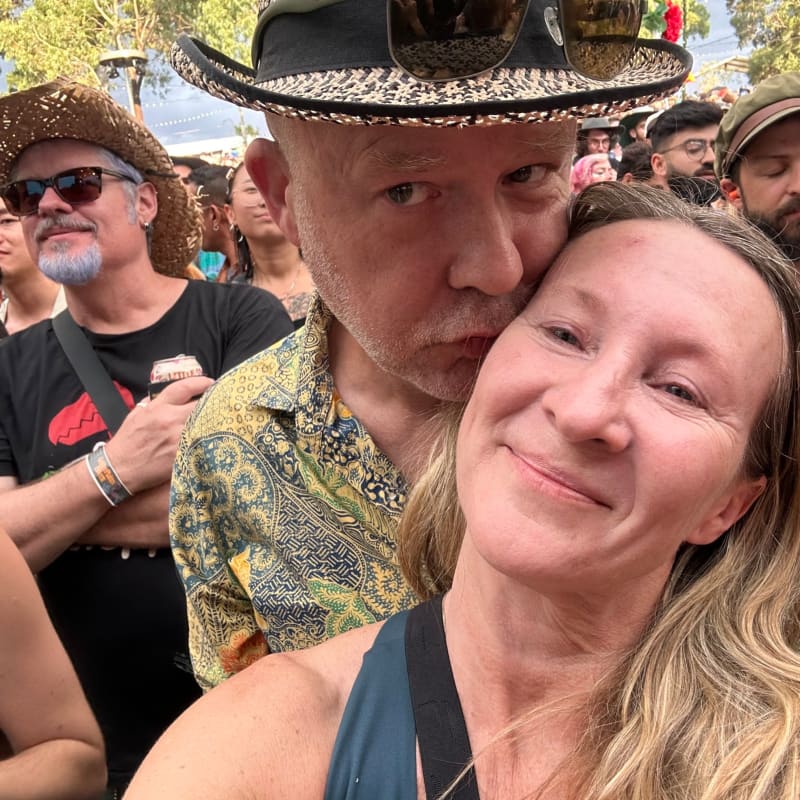 A man in a hat kisses the cheek of a woman with long blonde hair.