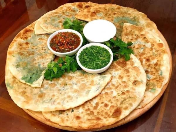 Crispy, golden Afghan flatbread stuffed with green veggies on a plate, with dipping sauces in bowls in the middle.
