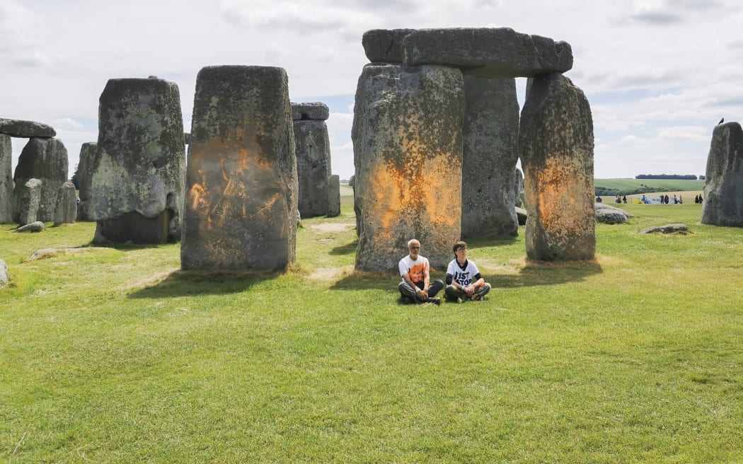 In this handout photo, Just Stop Oil protesters sit after spraying an orange substance on Stonehenge, in Salisbury, England, Wednesday June 19, 2024. (Just Stop Oil via AP)