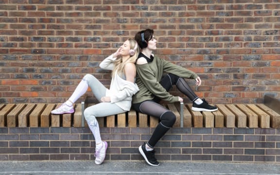 Friends relaxing, two girls listening to music on headphones on a street.