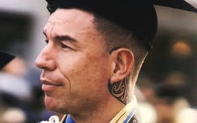 Levi Armstrong is dressed in graduation robes and the classic graduate hat. It's a close up of his face. He is looking towards the left side of the frame.