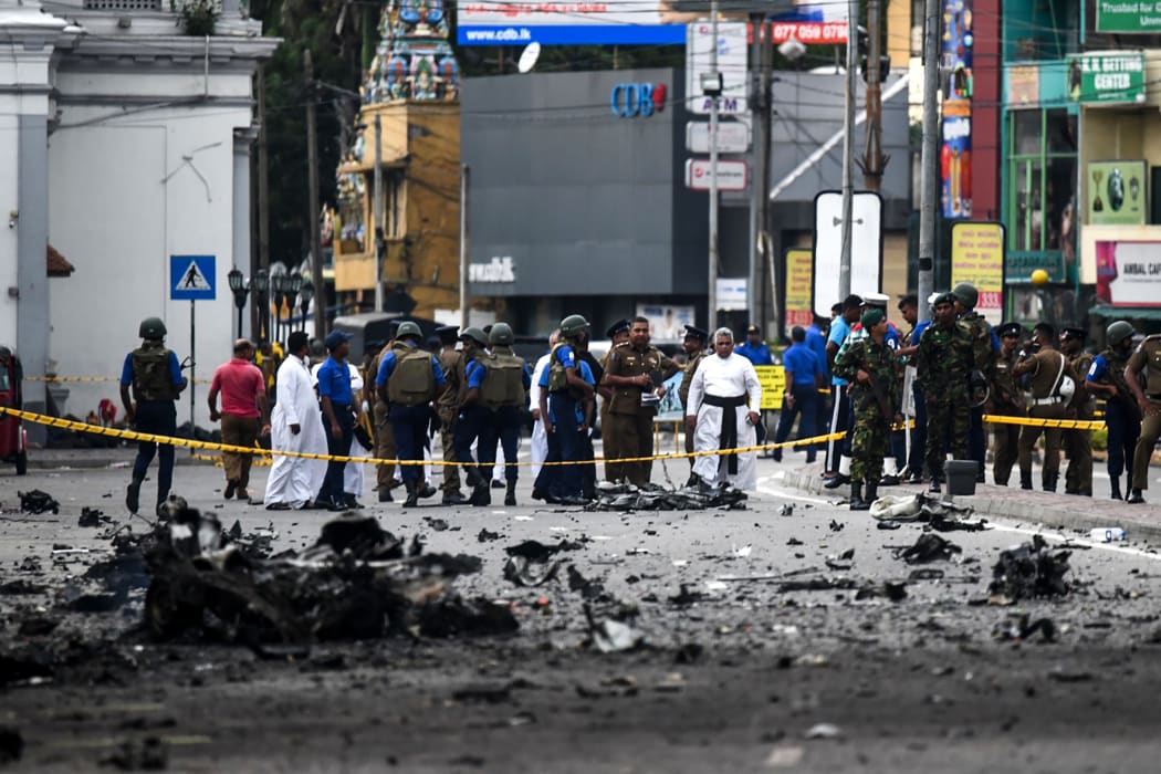 Sri Lankan security personnel inspect the debris of a car after it explodes when police tried to defuse a bomb near St. Anthony's Shrine as priests look on in Colombo on April 22, 2019, a day after the series of bomb blasts targeting churches and luxury hotels in Sri Lanka.