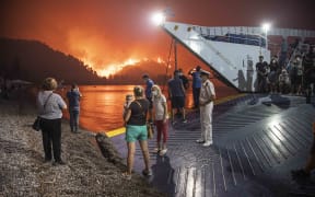 People board a ferry prior to an evacuation as a wildfire approaches the seaside village of Limni, on the island of Evia, Greece.