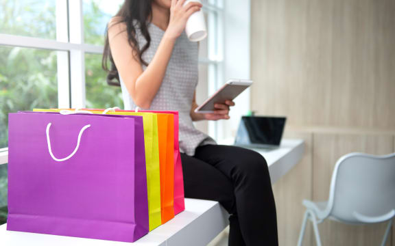 Woman is drinking a coffee and wilding the tablet phone with shopping bag at side for online shopping concept