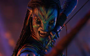 Neytiri has a multi-coloured face and a defensive snarl revealing sharp teeth.