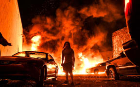 A man tries to toe away a car in a safe zone as the other car catches fire in a local parking garage on May 29, 2020 in Minneapolis, Minnesota, during a protest over the death of George Floyd, an unarmed black man,