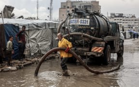 A Palestinian man clears stagnant water from the road near a displacement camp after the first winter rainfall in Gaza City on Friday.