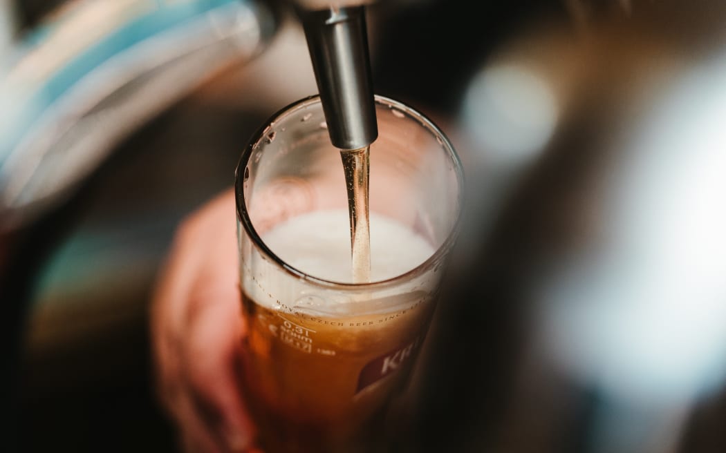 A person's hand can be seen holding a beer glass as the beer pours from a tap in a bar.