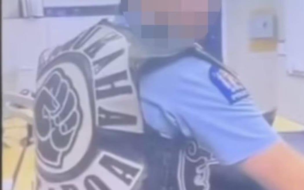 A screenshot of a Facebook post showing a police officer wearing a Mangu Kaha gang patch in the office.