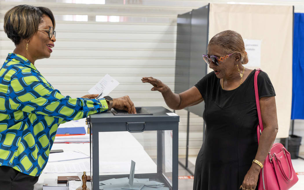 A scrutineer helps a voter to cast her ballot during the second round of France's legislative election at a polling station in Cayenne town hall in the French overseas department and region (DROM) of Guiana, on July 6, 2024. (Photo by Jody AMIET / AFP)