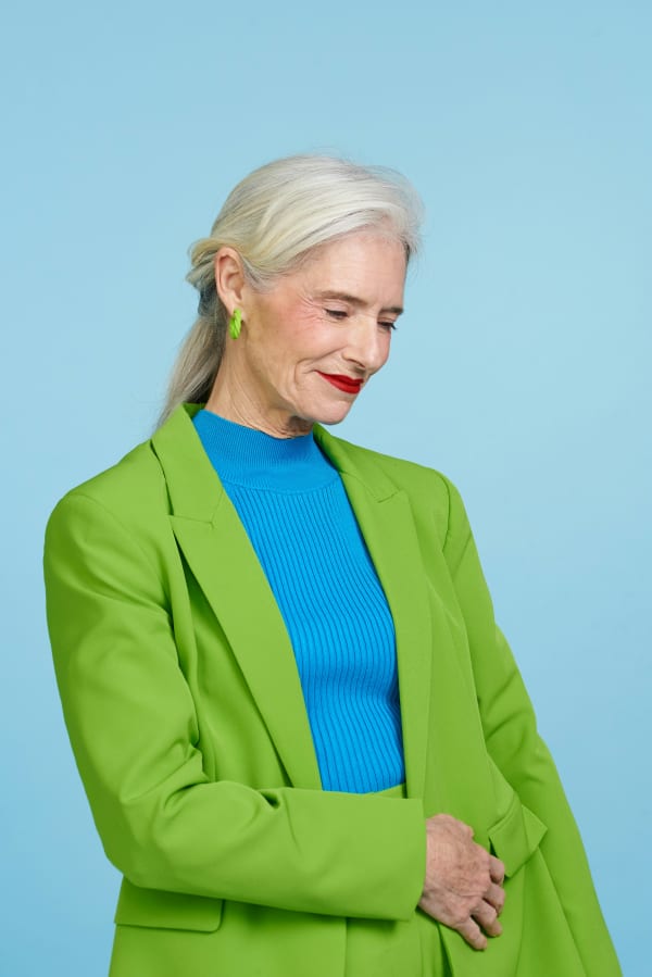 A smiling grey-haired woman in red lipstick and a bright green blazer.