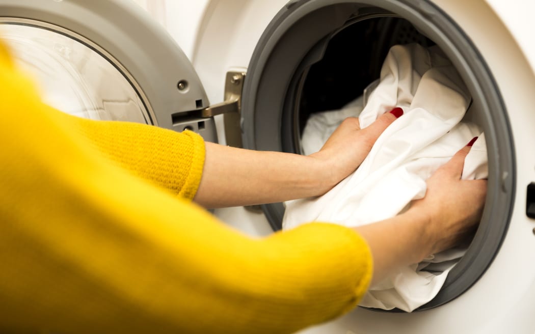 Woman hand loading dirty clothes in washing machine.