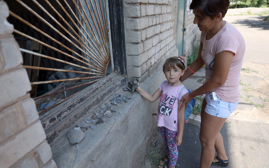 Tetyana and her five-year-old daughter show fragments of shells in an empty street in the town of Soledar, Donetsk region, on July 24, 2022, amid the Russian invasion of Ukraine. - There is little left of Soledar. A church, a few food shops and an ironmonger in a basement. Located right next to the front line, this mining town in eastern Ukraine's Donetsk region -- where several thousand people still live -- has been under constant shelling for more than three months. (Photo by Anatolii Stepanov / AFP)