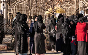 Afghan female university students stop by Taliban security personnel stand next to a university in Kabul on December 21, 2022.
