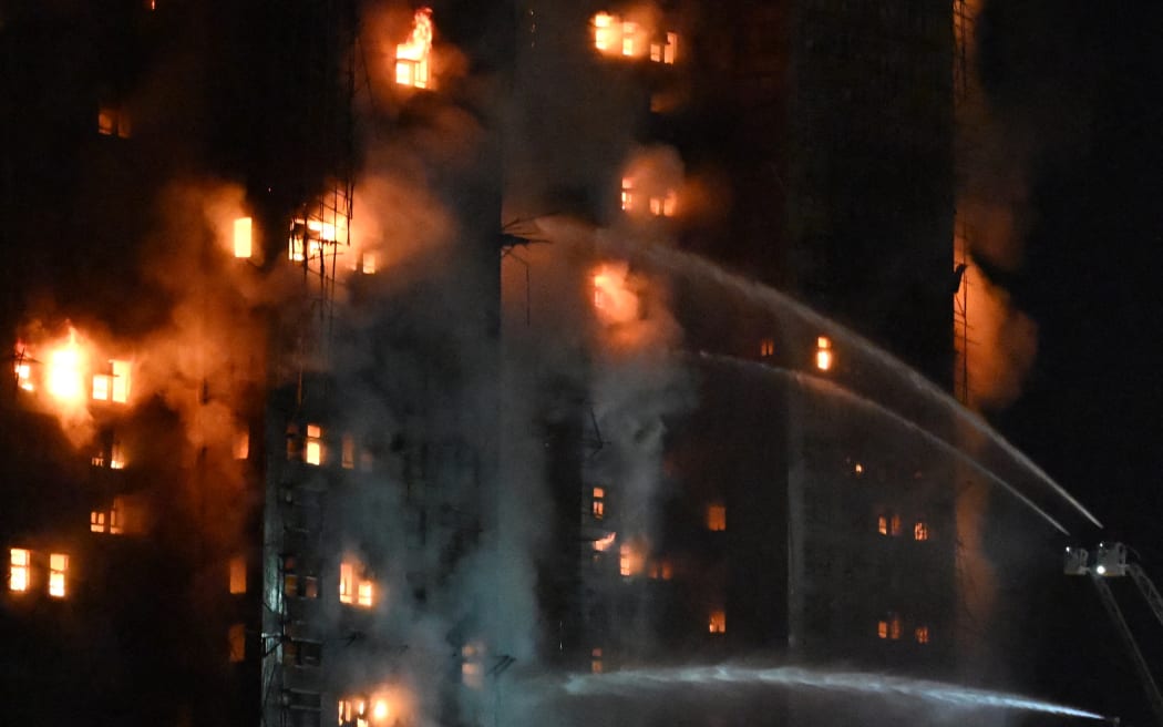 Firefighters spray water during a major fire at the Wang Fuk Court residential estate in Hong Kong's Tai Po district on November 26, 2025. At least four people were killed when a fire engulfed several high-rise blocks in a Hong Kong residential estate on November 26, the government said, with media reporting that some residents were trapped inside. (Photo by Peter PARKS / AFP)