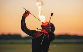Chris Blaze, known as The Fire Ninja, pictured fire breathing in front of a sunset.