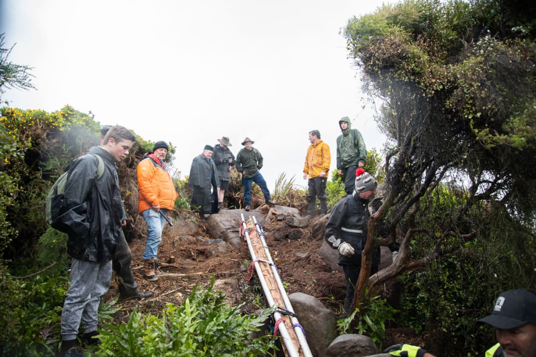 Volunteers help to carry the McKenzie Brothers Flag Pole down from Bluff Hill