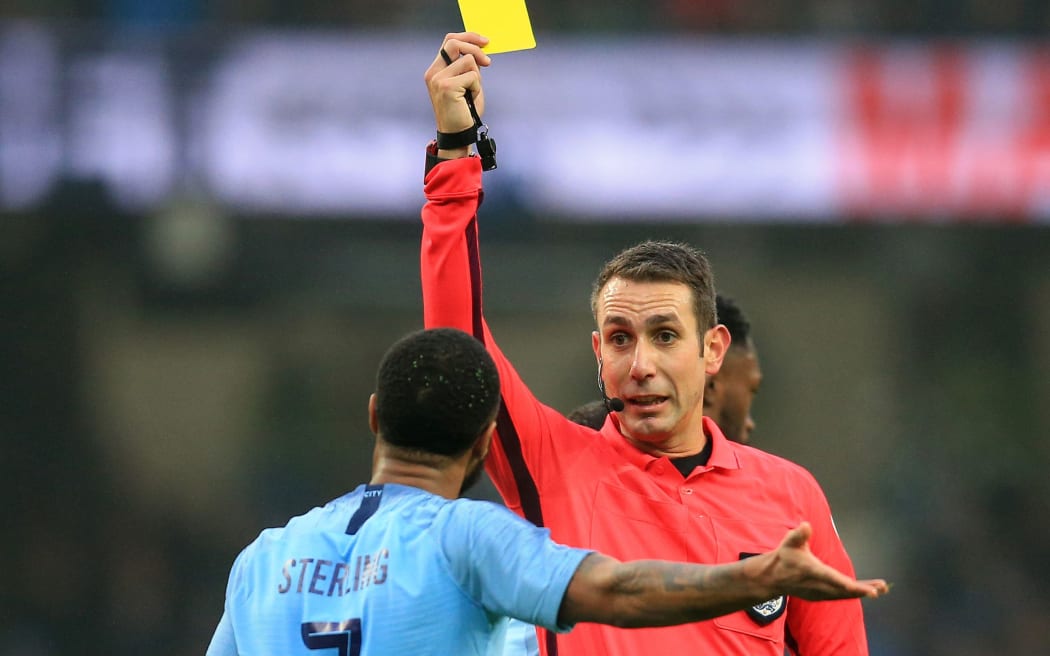 English football referee David Coote shows a yellow card.