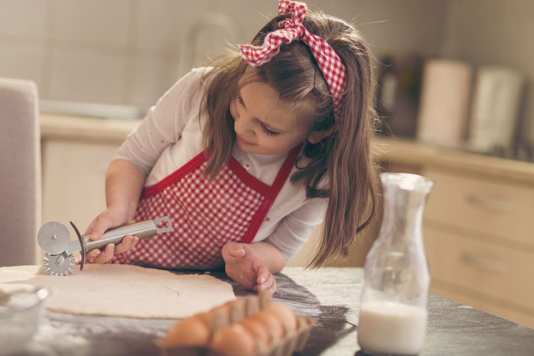 Little girl with apron in kitchen cutting dough.