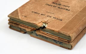 This is an image of two WW2 pilots log books. They both have a big cut through the top. They are placed on top of each other so that it's possible to see the damage lined up.