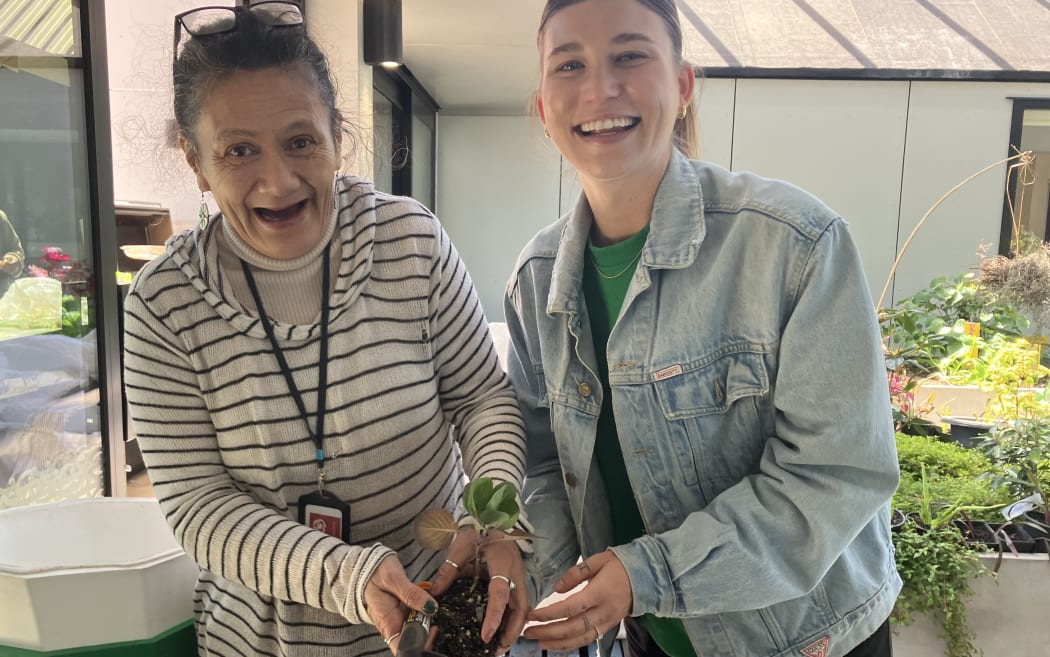 Shirleen and Nic smile broadly. Shirleen is holding a trowel and seedling.