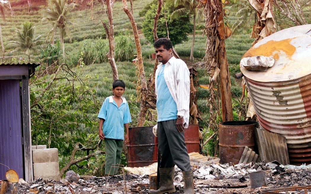 Two neighbours survey the ruins of a Fiji-Indian house torched by rebels in Waidalice, an area with strong support for coup leader George Speight, 80 kms north of Suva, 07 August 2000.  Fijian-Indians, victims of wide spread violence since the coup, are still living in fear for their safety despite Speight being detained on the prison island of Nukulau.  (ELECTRONIC IMAGE)  AFP PHOTO/William WEST (Photo by WILLIAM WEST / AFP)