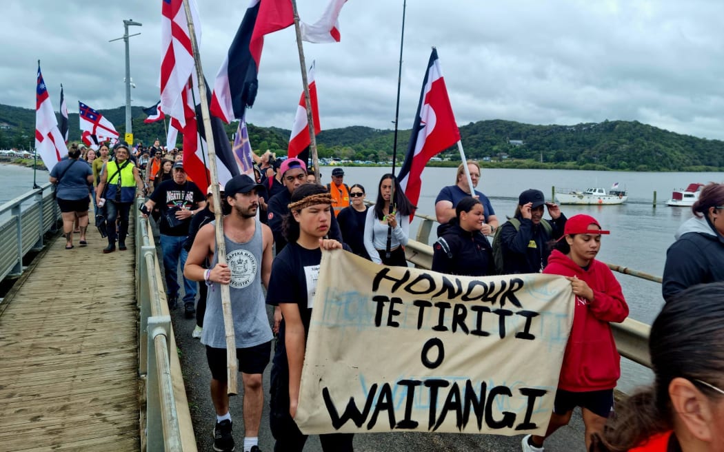 People holding a 'Honour Te Tiriti o Waitangi' sign at Waitangi.