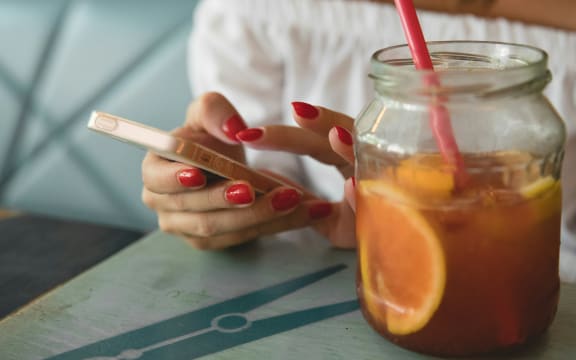 A woman with red fingernails scrolls on a phone accompanied by an orange juice drink.