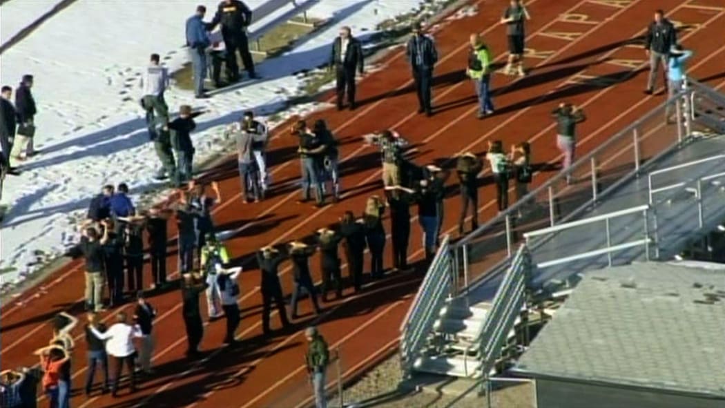 TV news footage shows students lining up to be checked by police at a running track.