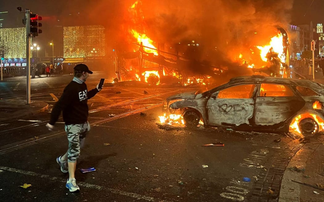 Flames rise from a car and a bus, set alight at the junction of Bachelors Walk and the O'Connell Bridge, in Dublin on November 23, 2023, as people took to the streets in protest following the stabbings earlier in the day. Protesters in Dublin on Thursday torched a car and fought police, an AFP journalist reported, after three children were injured in a suspected school stabbing that social media rumours attributed to a foreign national. (Photo by Peter MURPHY / AFP)