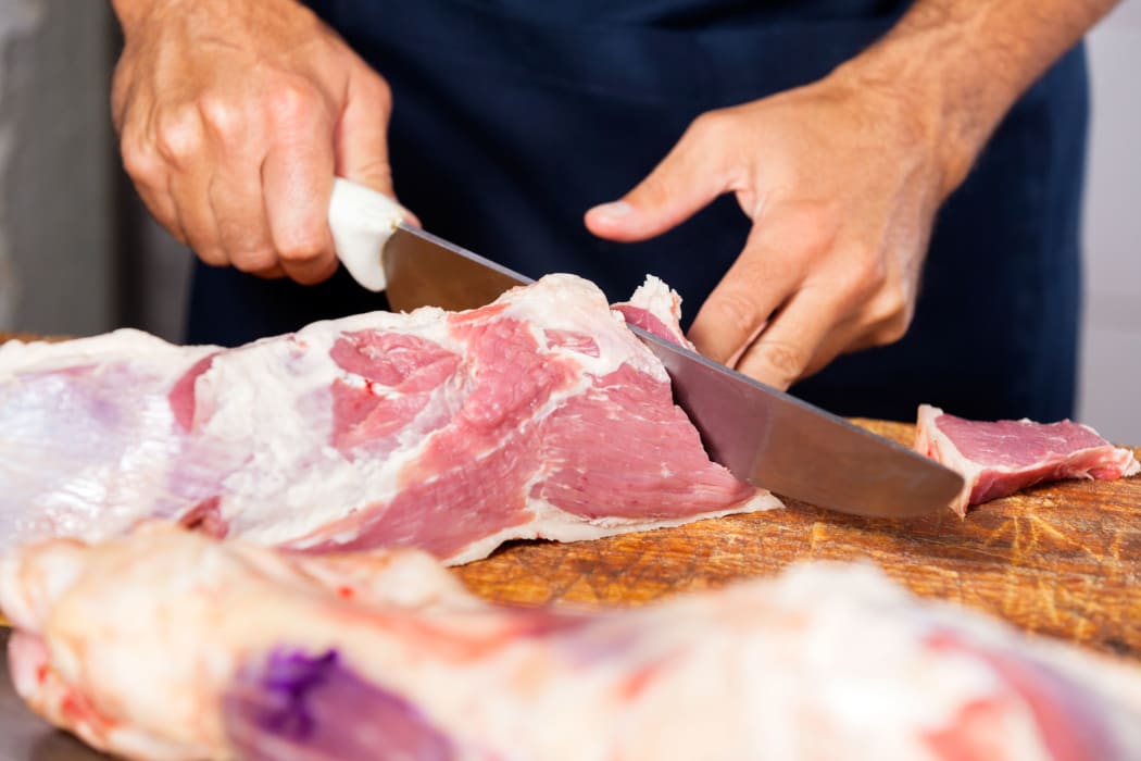 Cropped image of male butcher cutting raw meat with knife at counter in shop