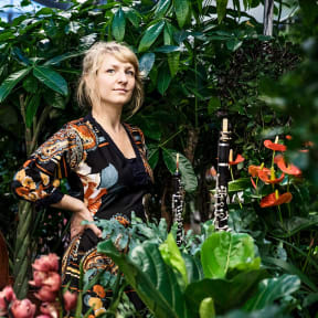 Promo shot of Swedish composer Andrea Tarrodi. She stands surrounded by greenery and musical instruments
