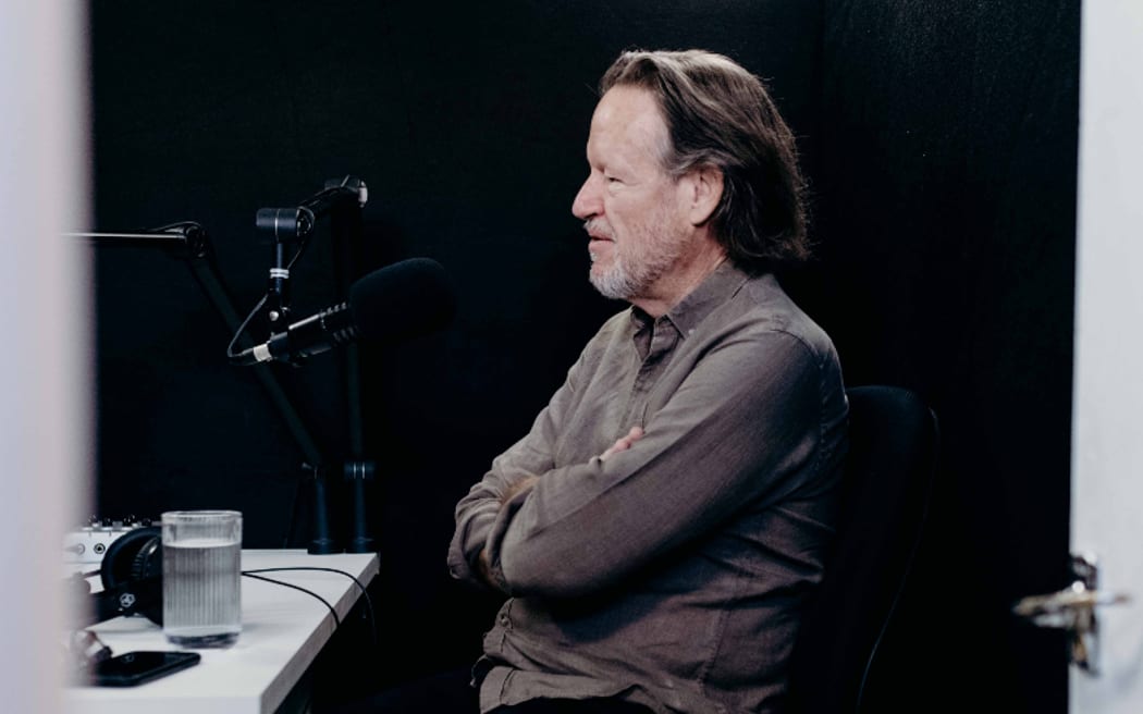 NZ Herald Journalist Simon Wilson sitting, arms crossed, in front of a microphone.