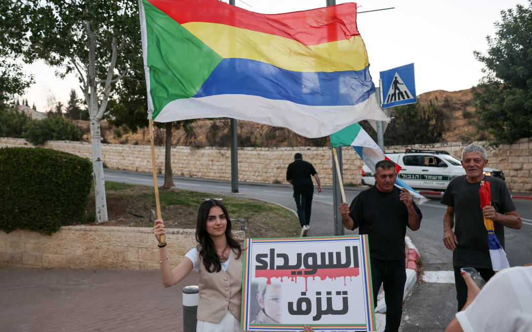 Members of the Druze community in Israel and their supporters wave a Druze flag and raise a placard near the US Embassy in Jerusalem to show solidarity with their community in neighbouring Syria, on July 16, 2025. The clashes began on July 13 between the Druze and Bedouin tribes in soutern Syria's Sweida city, who have a long-running feud, sparking an intervention by government forces. (Photo by AHMAD GHARABLI / AFP)