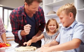 A photo of a father making pizza with kids